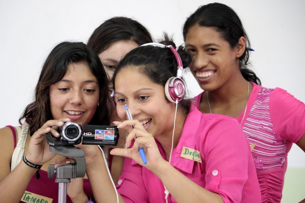 Photo of four young women smiling and looking through a video camera